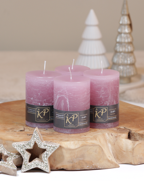 Vier Tischkerzen in altrosa dekorativ auf einem Holztisch mit Weihnachtsdeko im Hintergrund.