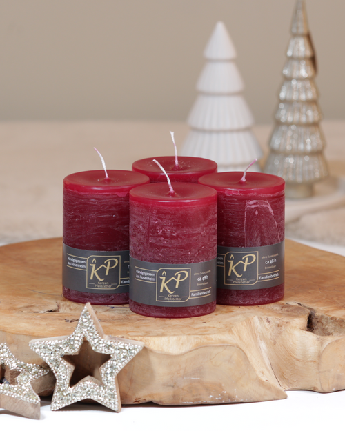 Vier Tischkerzen in burgundrot dekorativ auf einem Holztisch mit Weihnachtsdeko im Hintergrund.