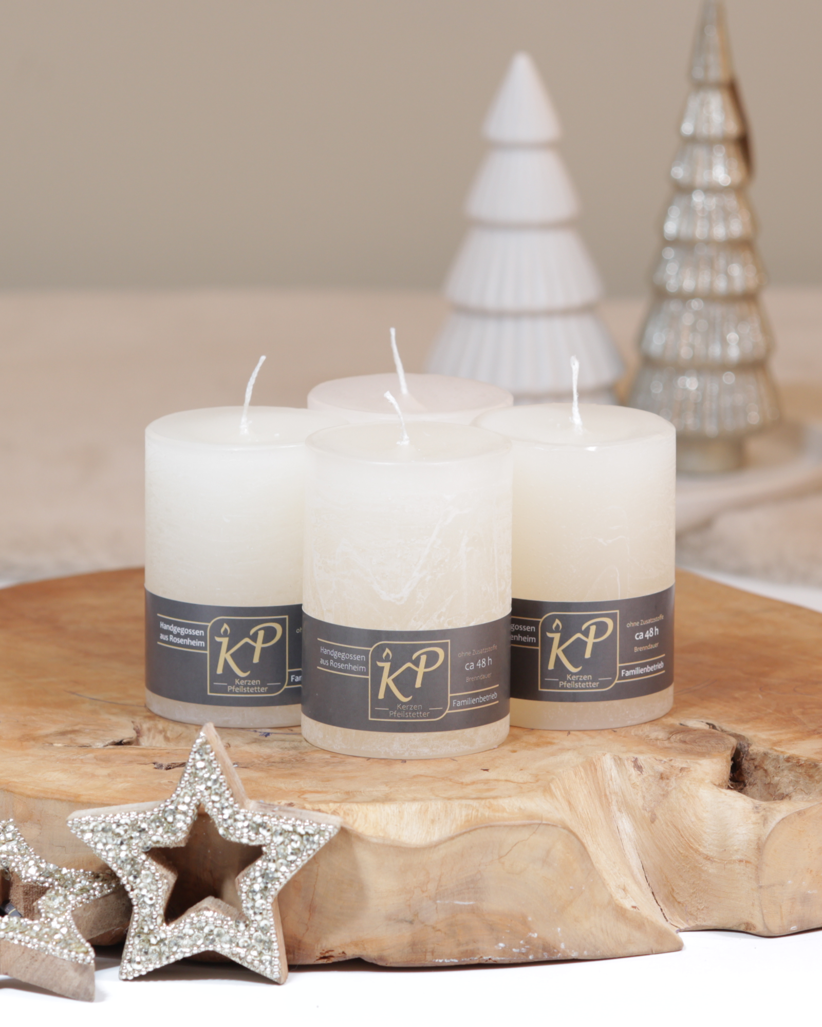 Vier Tischkerzen in creme dekorativ auf einem Holztisch mit Weihnachtsdeko im Hintergrund.