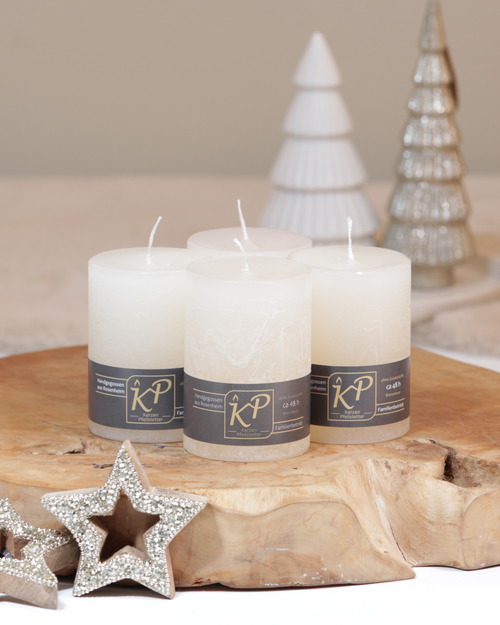 Vier Tischkerzen in creme dekorativ auf einem Holztisch mit Weihnachtsdeko im Hintergrund.