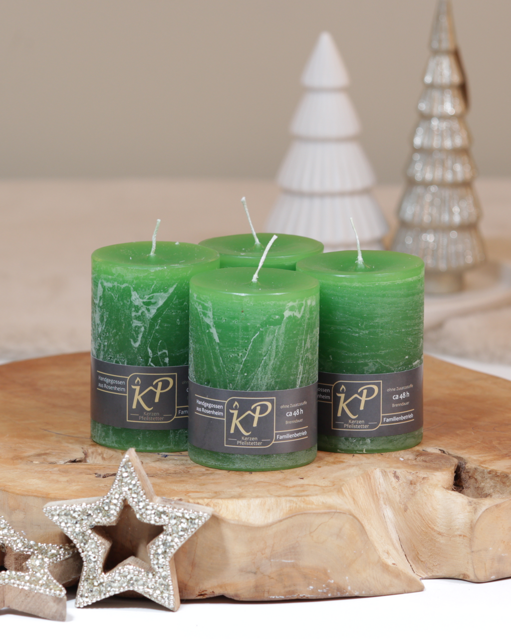 Vier Tischkerzen in grün dekorativ auf einem Holztisch mit Weihnachtsdeko im Hintergrund.
