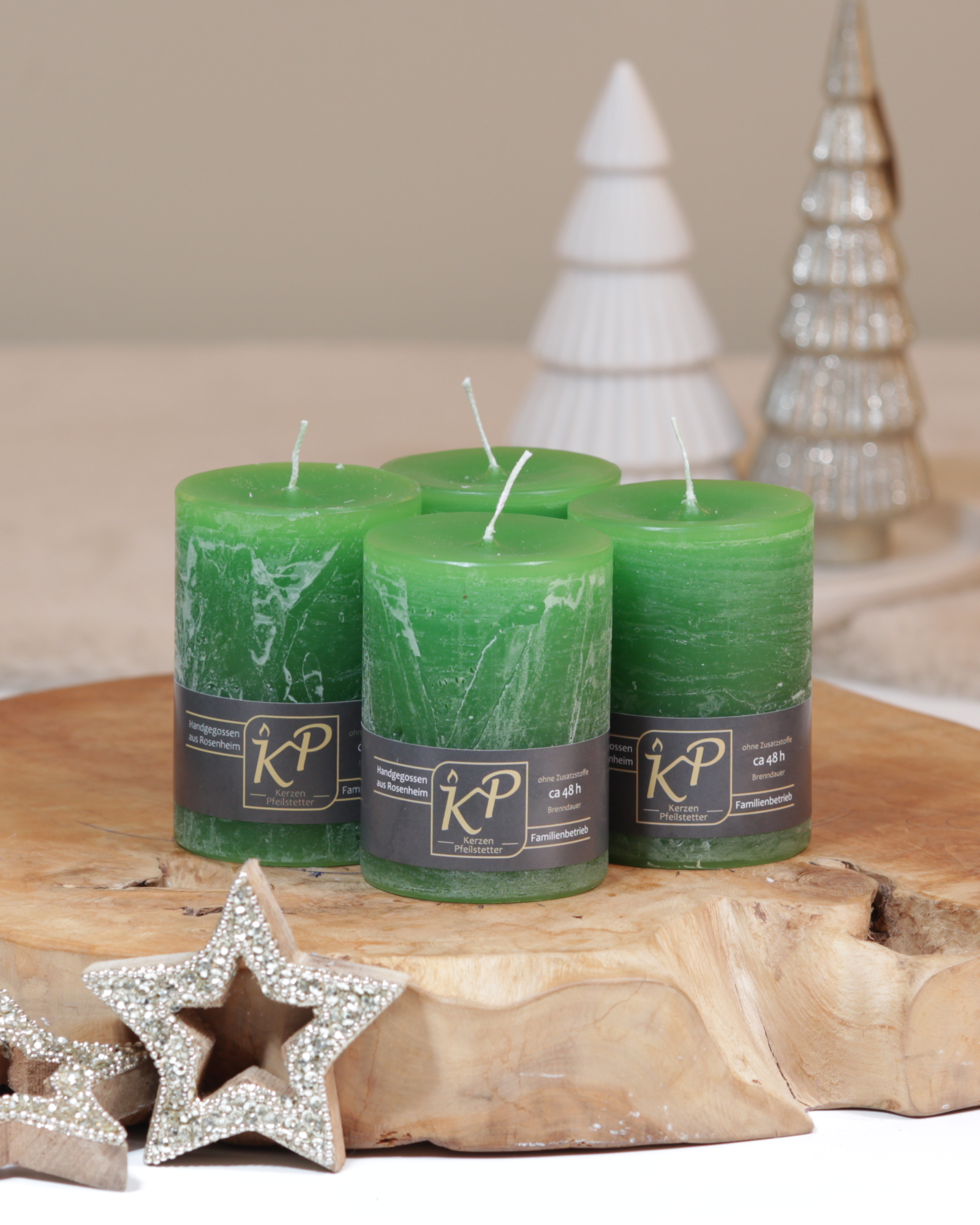Vier Tischkerzen in grün dekorativ auf einem Holztisch mit Weihnachtsdeko im Hintergrund.