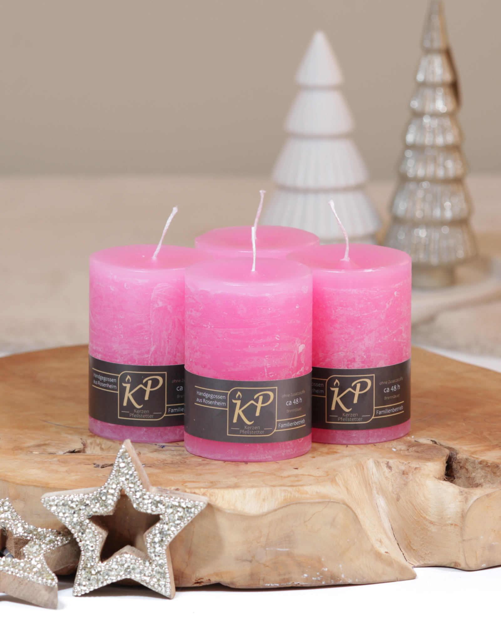 Vier Tischkerzen in hellrosa dekorativ auf einem Holztisch mit Weihnachtsdeko im Hintergrund.