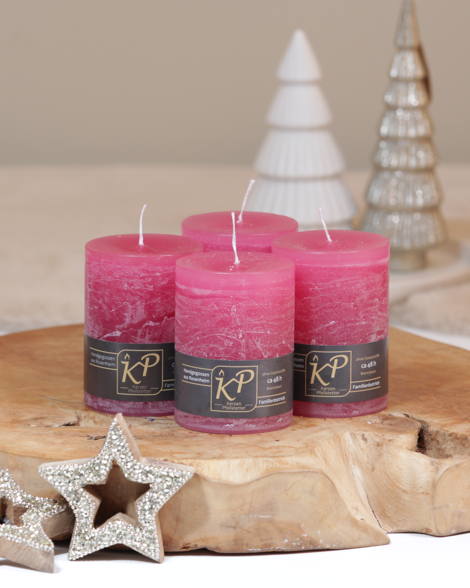 Vier Tischkerzen in himbeerrosa dekorativ auf einem Holztisch mit Weihnachtsdeko im Hintergrund.