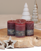 Vier Tischkerzen in kastanienbraun dekorativ auf einem Holztisch mit Weihnachtsdeko im Hintergrund.