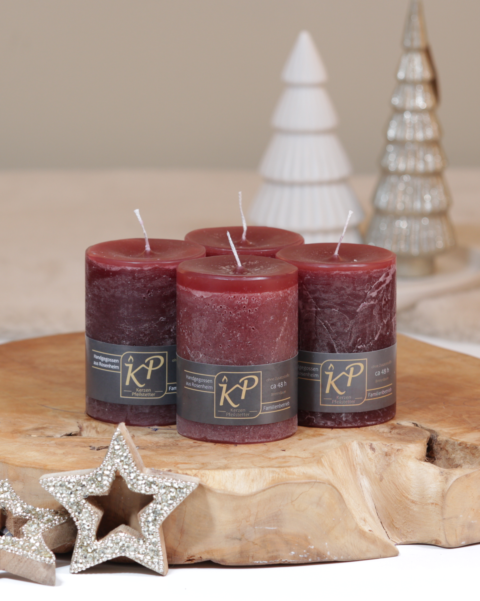 Vier Tischkerzen in kastanienbraun dekorativ auf einem Holztisch mit Weihnachtsdeko im Hintergrund.
