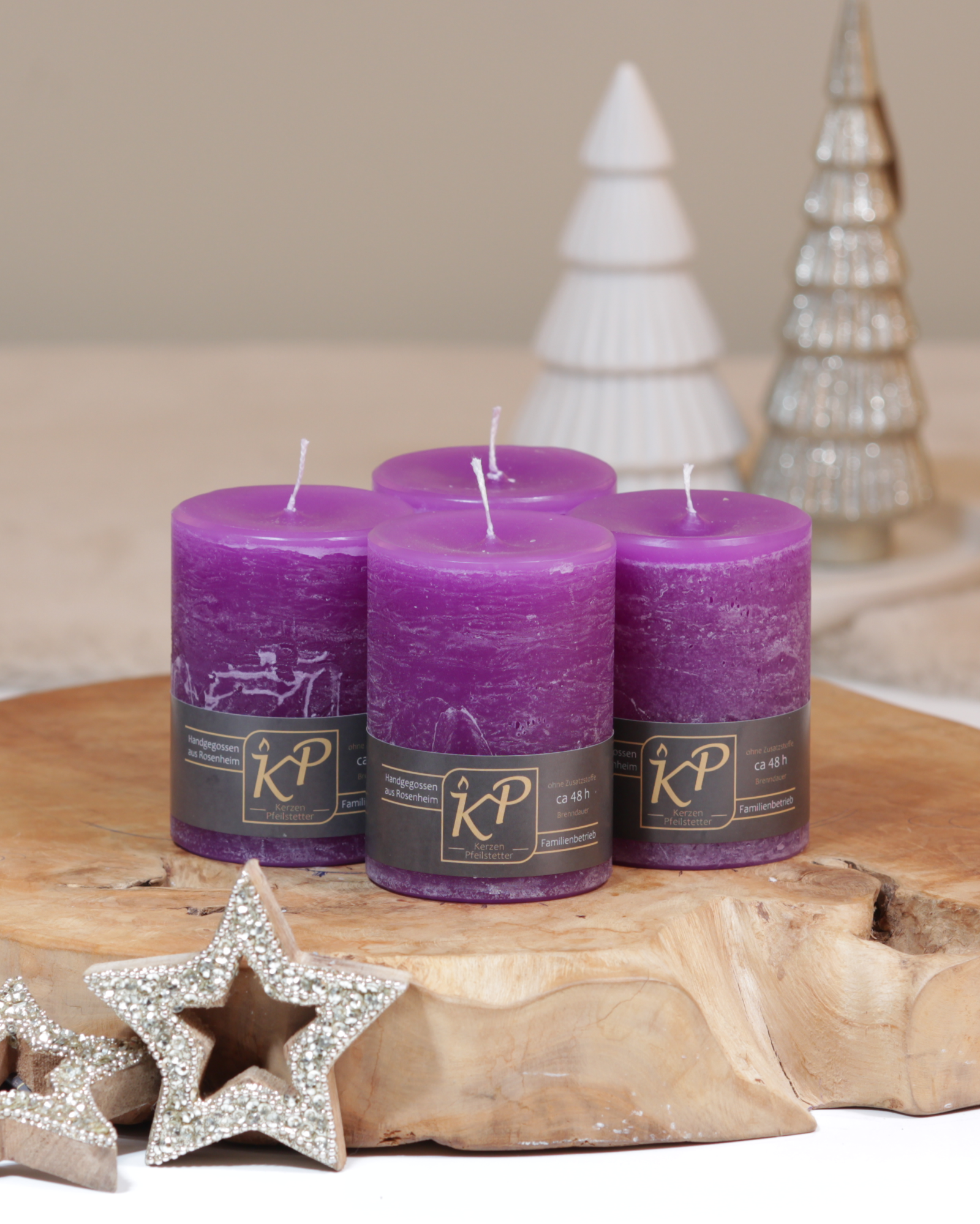 Vier Tischkerzen in lila dekorativ auf einem Holztisch mit Weihnachtsdeko im Hintergrund.
