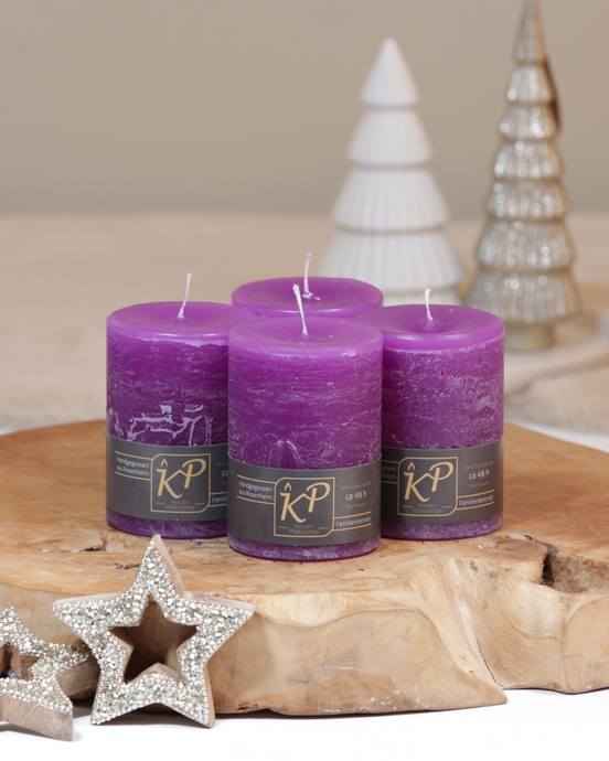 Vier Tischkerzen in lila dekorativ auf einem Holztisch mit Weihnachtsdeko im Hintergrund.