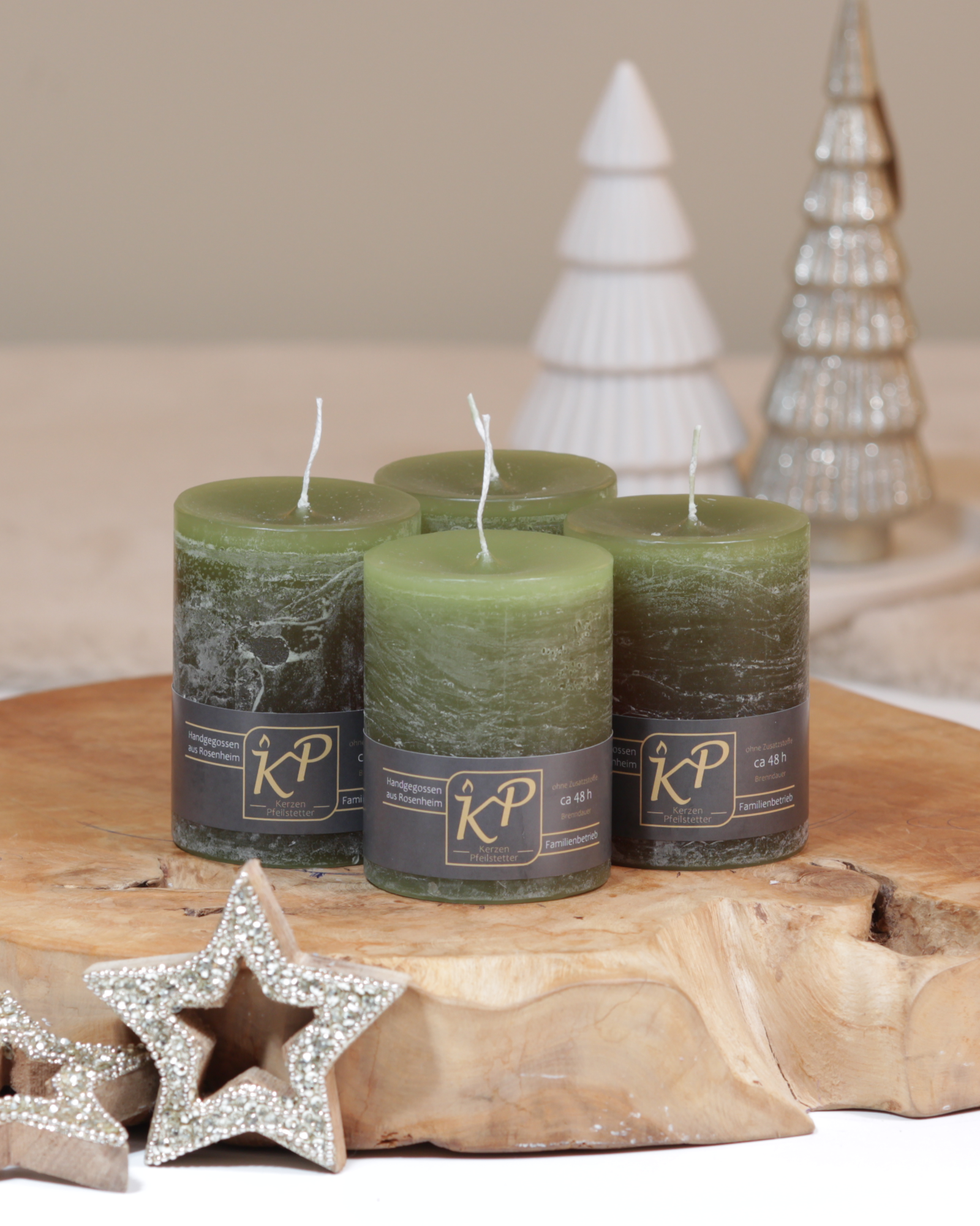Vier Tischkerzen in olivgrün dekorativ auf einem Holztisch mit Weihnachtsdeko im Hintergrund.