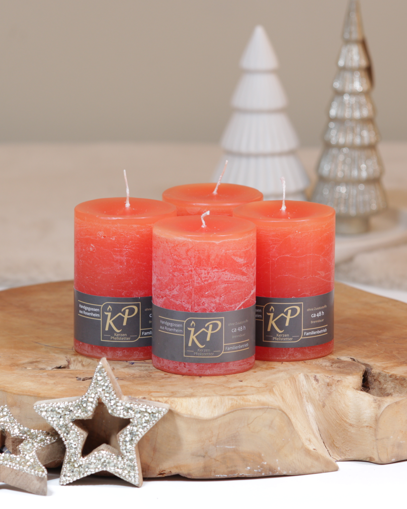 Vier Tischkerzen in orange dekorativ auf einem Holztisch mit Weihnachtsdeko im Hintergrund.