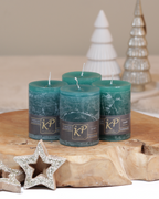 Vier Tischkerzen in ozeangrün dekorativ auf einem Holztisch mit Weihnachtsdeko im Hintergrund.