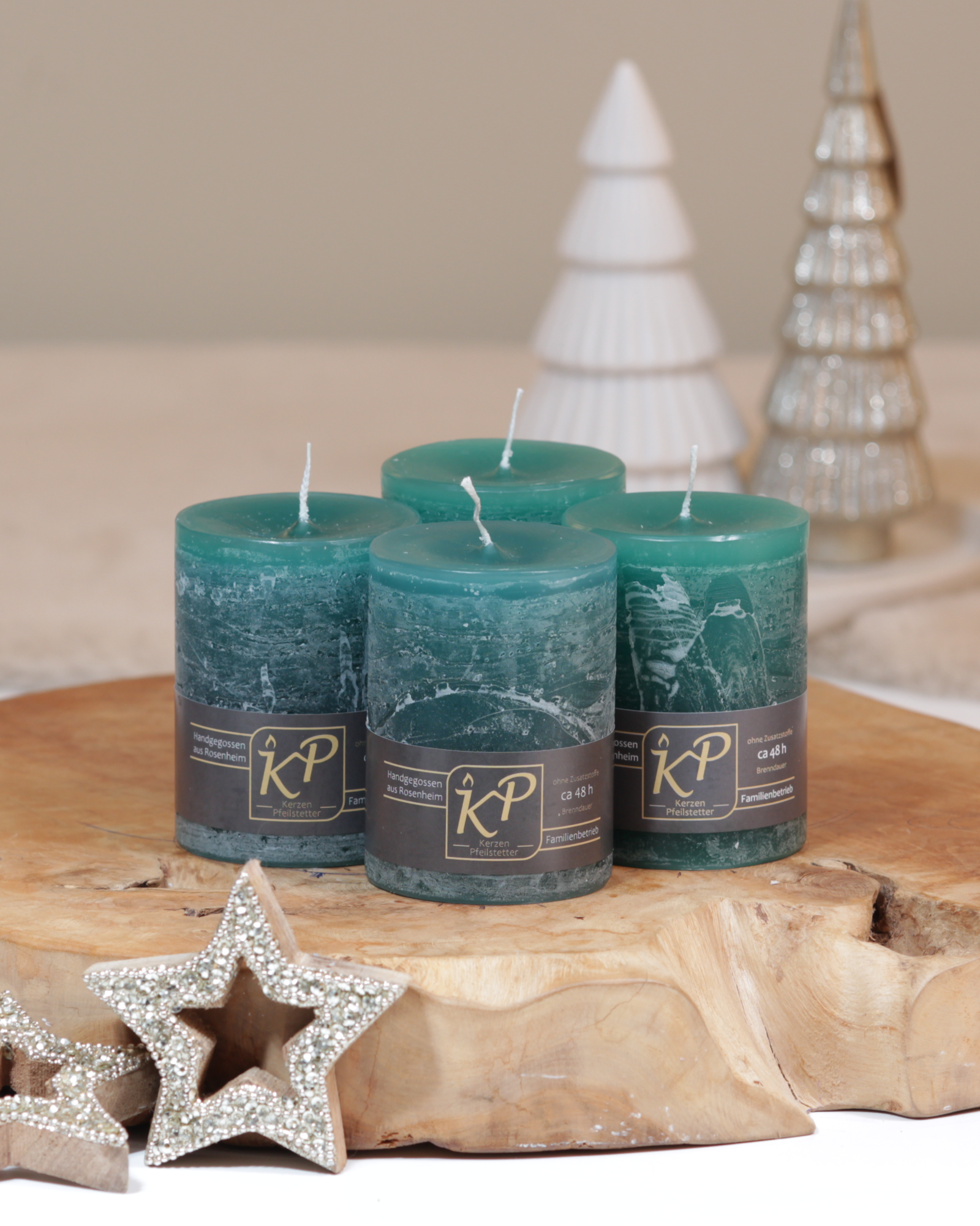 Vier Tischkerzen in ozeangrün dekorativ auf einem Holztisch mit Weihnachtsdeko im Hintergrund.