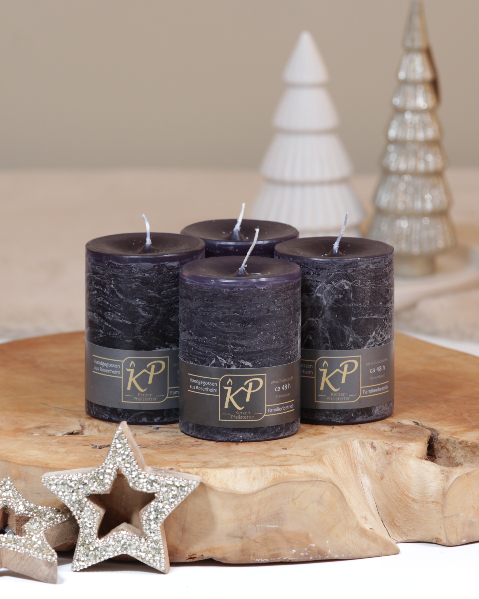 Vier Tischkerzen in schwarz dekorativ auf einem Holztisch mit Weihnachtsdeko im Hintergrund.