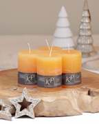 Vier Tischkerzen in sonnengelb dekorativ auf einem Holztisch mit Weihnachtsdeko im Hintergrund.
