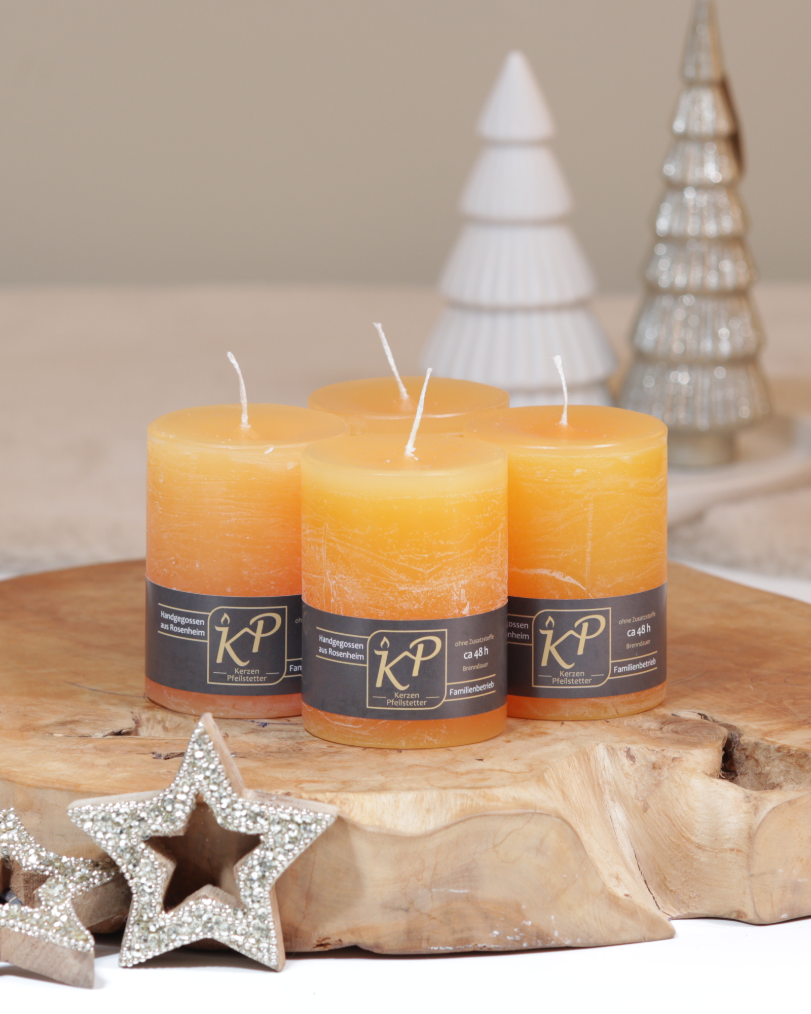 Vier Tischkerzen in sonnengelb dekorativ auf einem Holztisch mit Weihnachtsdeko im Hintergrund.