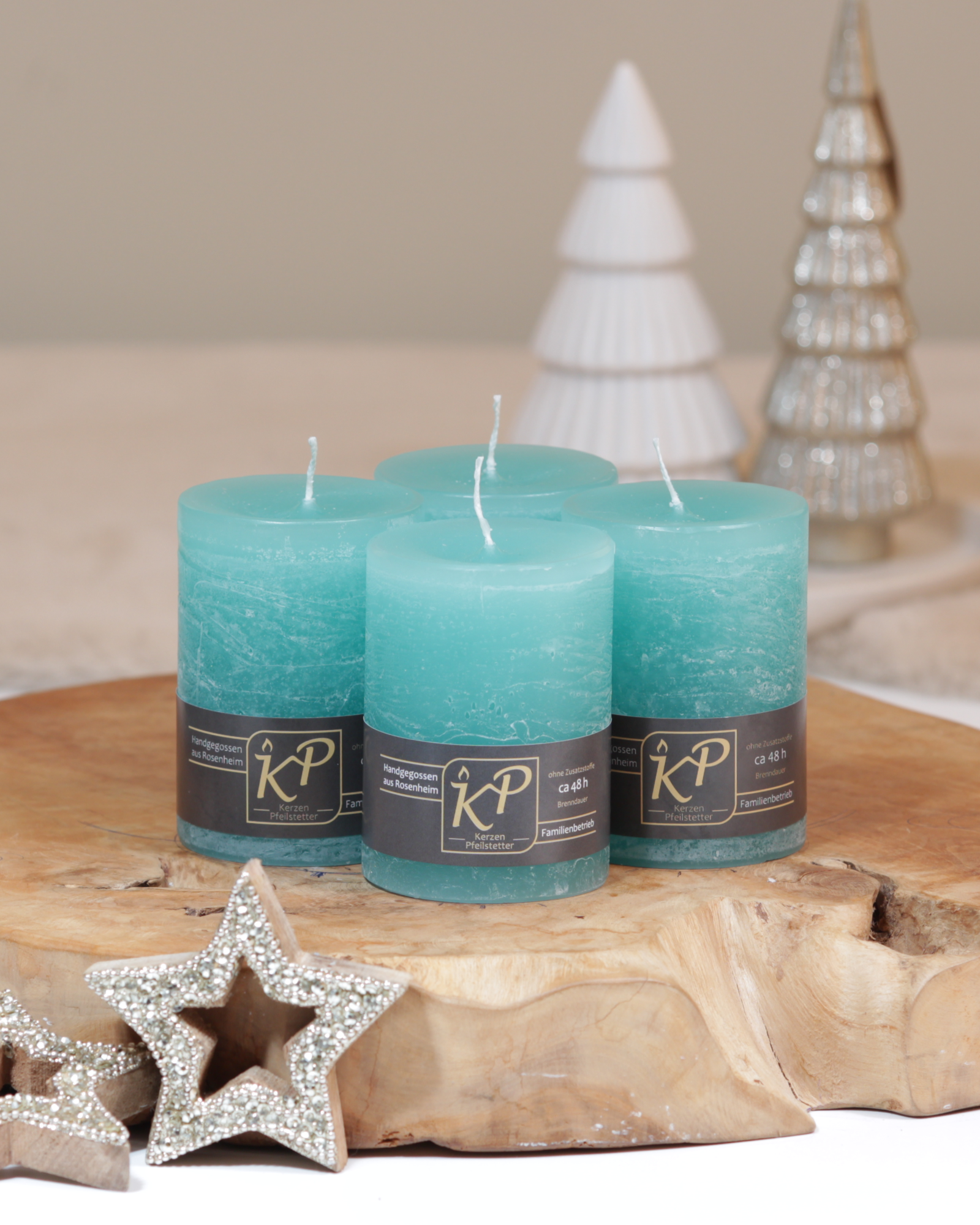Vier Tischkerzen in türkis dekorativ auf einem Holztisch mit Weihnachtsdeko im Hintergrund.