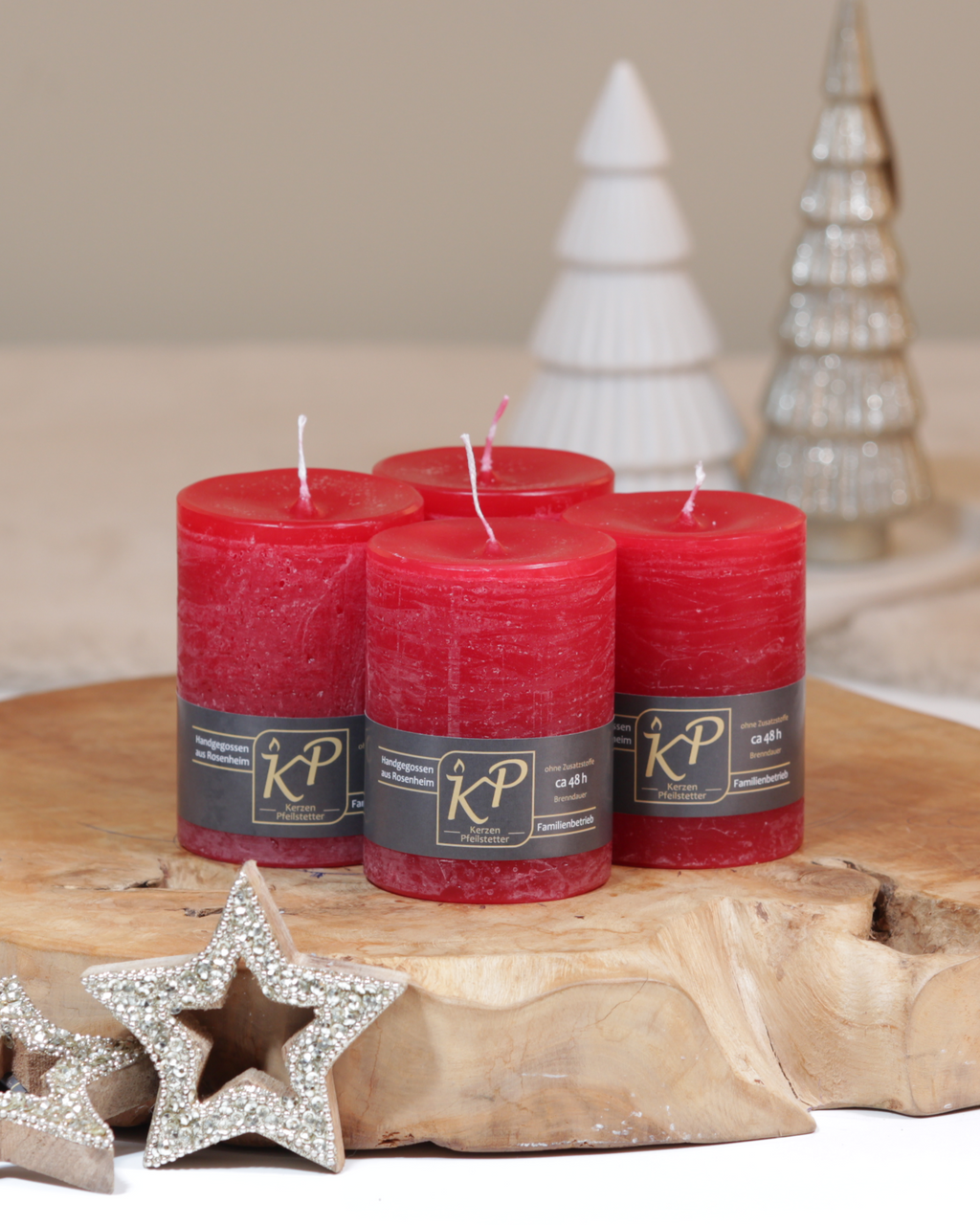Vier Tischkerzen in weihnachtsrot dekorativ auf einem Holztisch mit Weihnachtsdeko im Hintergrund.
