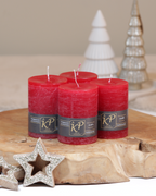 Vier Tischkerzen in weihnachtsrot dekorativ auf einem Holztisch mit Weihnachtsdeko im Hintergrund.