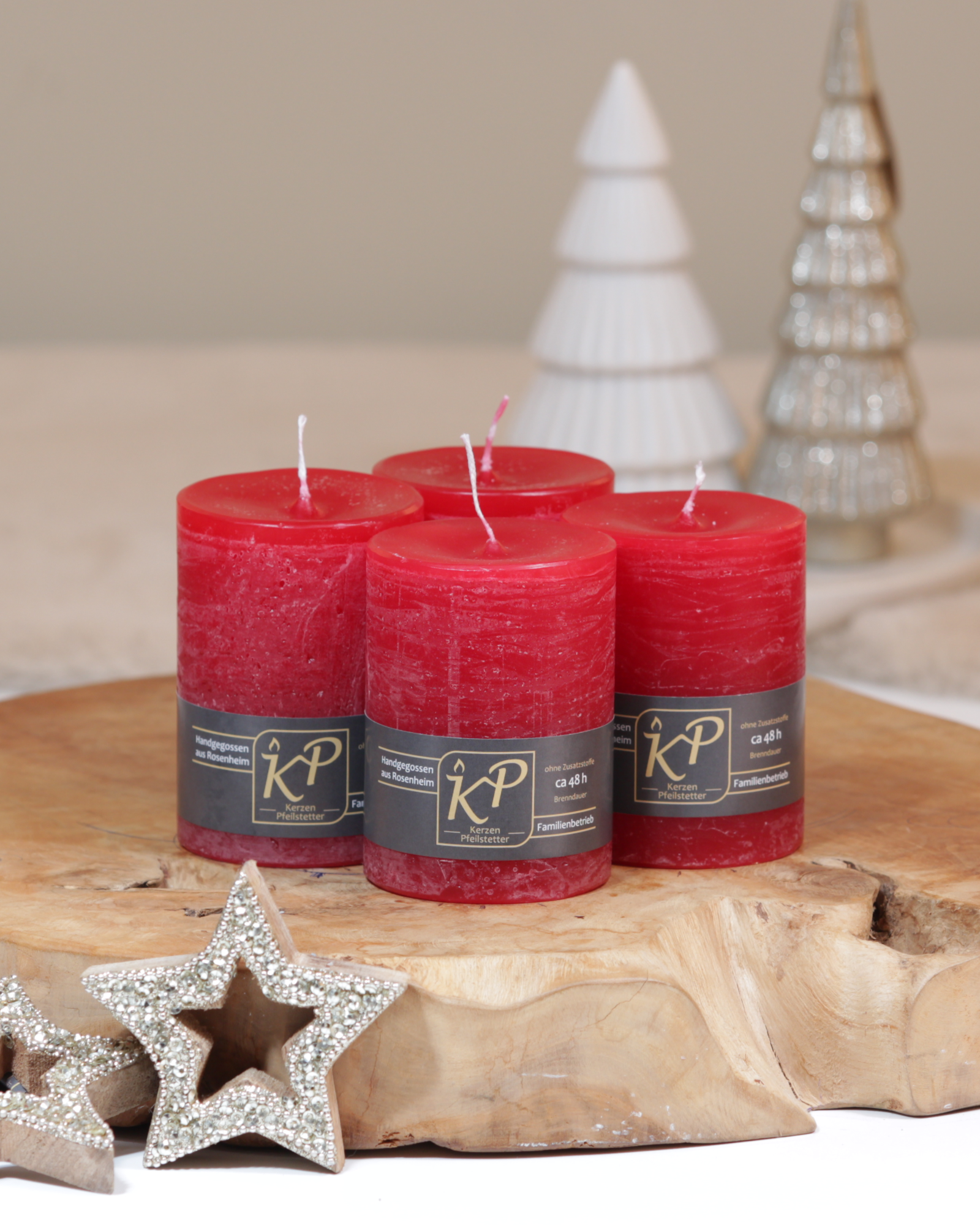 Vier Tischkerzen in weihnachtsrot dekorativ auf einem Holztisch mit Weihnachtsdeko im Hintergrund.