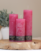 Blütenkerzen in himbeerrosa in drei Größen – dekorativ auf einem Holztisch mit Pflanze im Hintergrund.