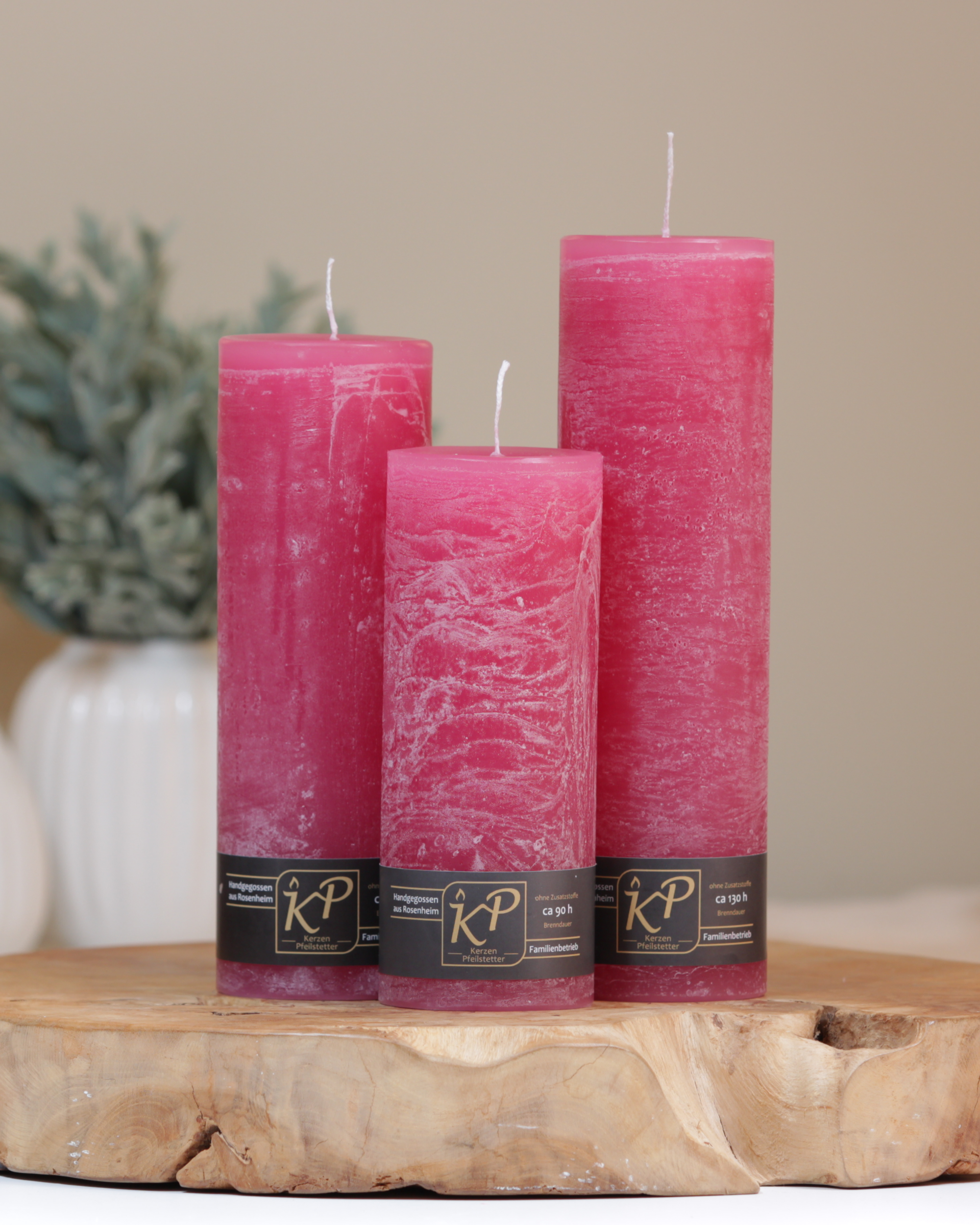 Blütenkerzen in himbeerrosa in drei Größen – dekorativ auf einem Holztisch mit Pflanze im Hintergrund.