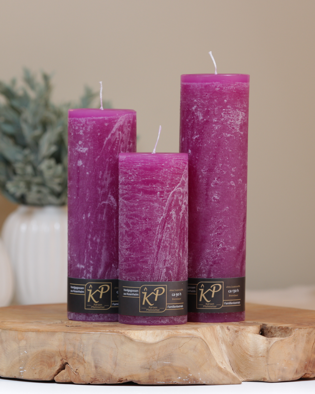 Blütenkerzen in magenta in drei Größen – dekorativ auf einem Holztisch mit Pflanze im Hintergrund.