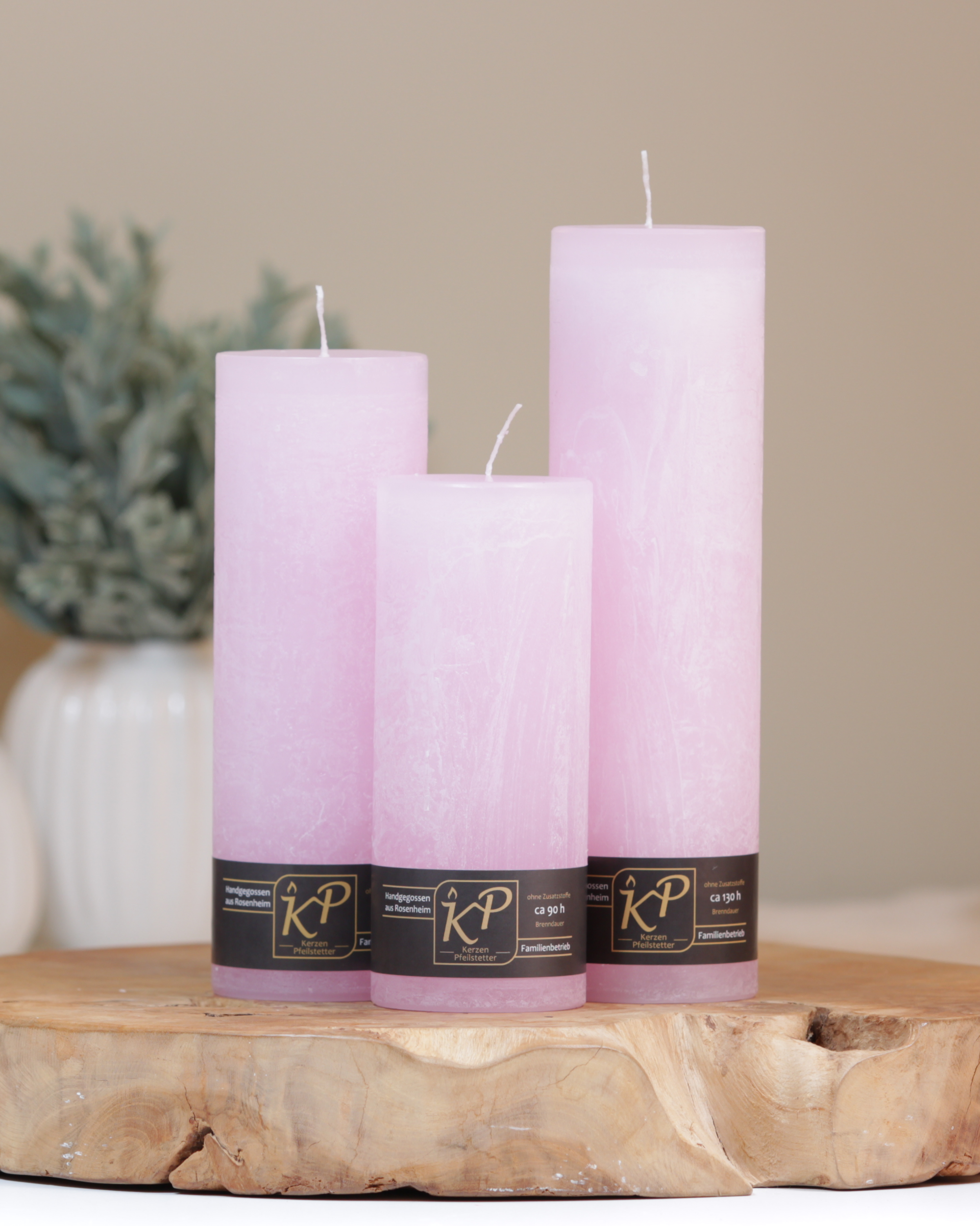 Blütenkerzen in pastellrosa in drei Größen – dekorativ auf einem Holztisch mit Pflanze im Hintergrund.