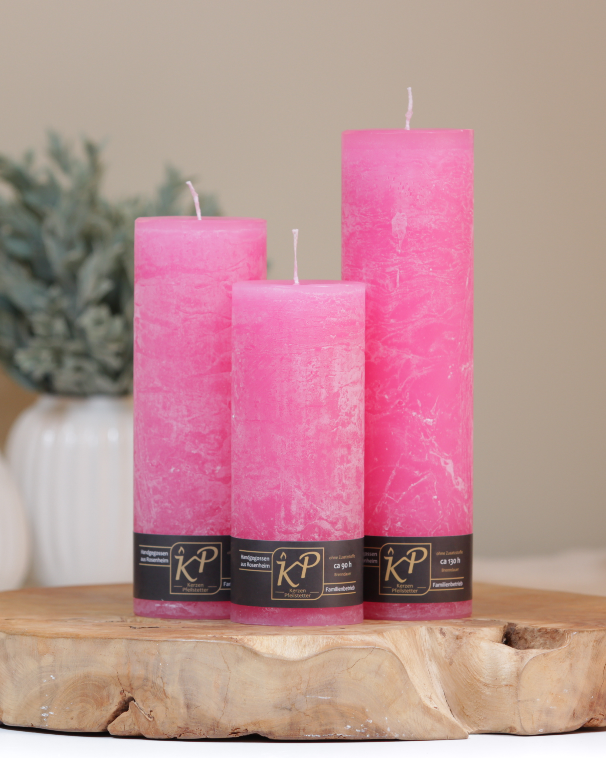Blütenkerzen in pink in drei Größen – dekorativ auf einem Holztisch mit Pflanze im Hintergrund.