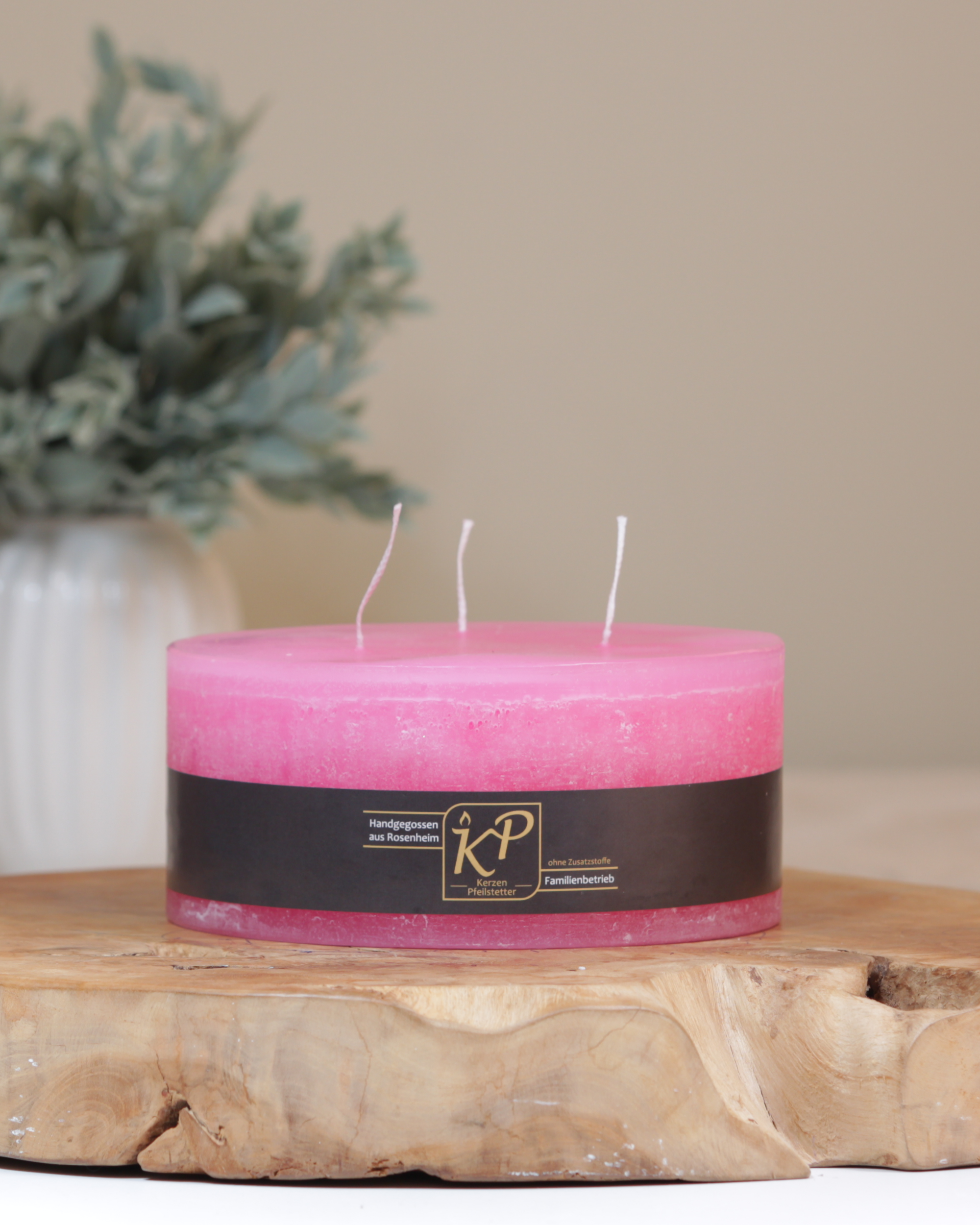 Dreidochtkerze in pink dekorativ auf einem Holztisch mit Pflanze im Hintergrund.