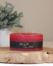 Dreidochtkerze in weihnachtsrot dekorativ auf einem Holztisch mit Pflanze im Hintergrund.