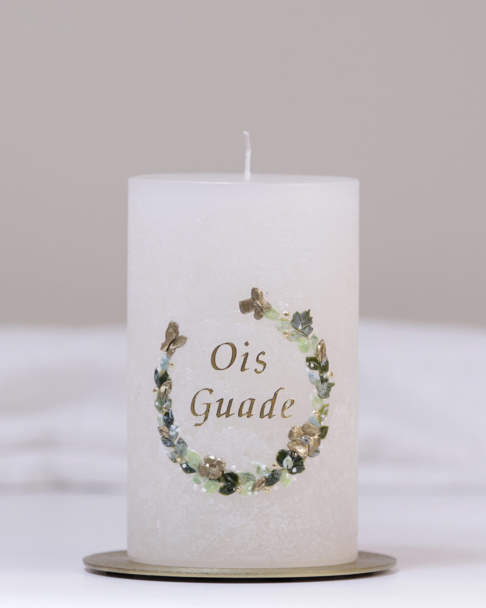 Geburtstagskerze in Elfenbein mit grün-goldenem Blumenkranz und dem Schriftzug ‚Ois Guade‘ – handgegossen und verziert.