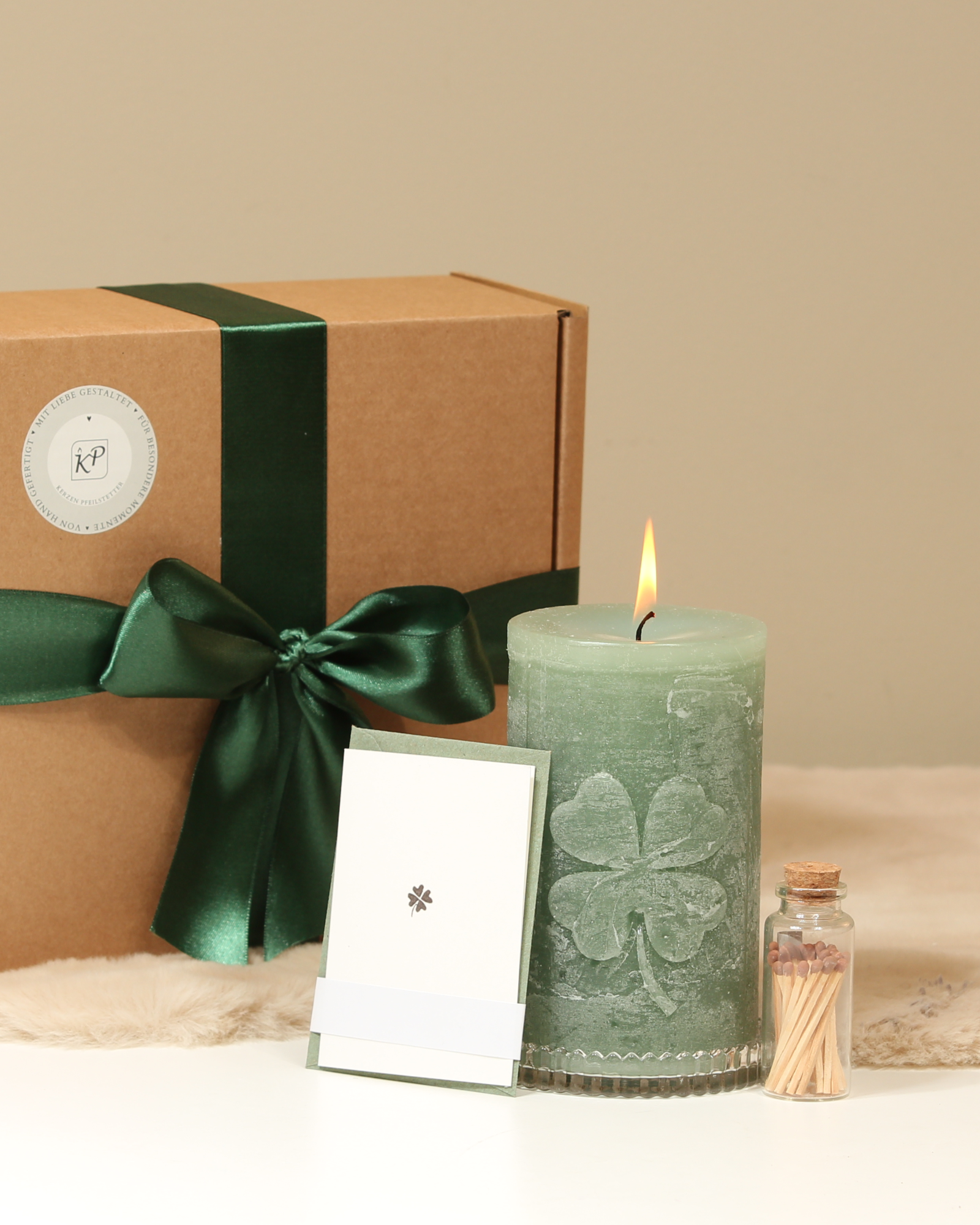 Geschenkbox Kleeblatt Salbeigrün mit Kerze und Zubehör davor präsentiert