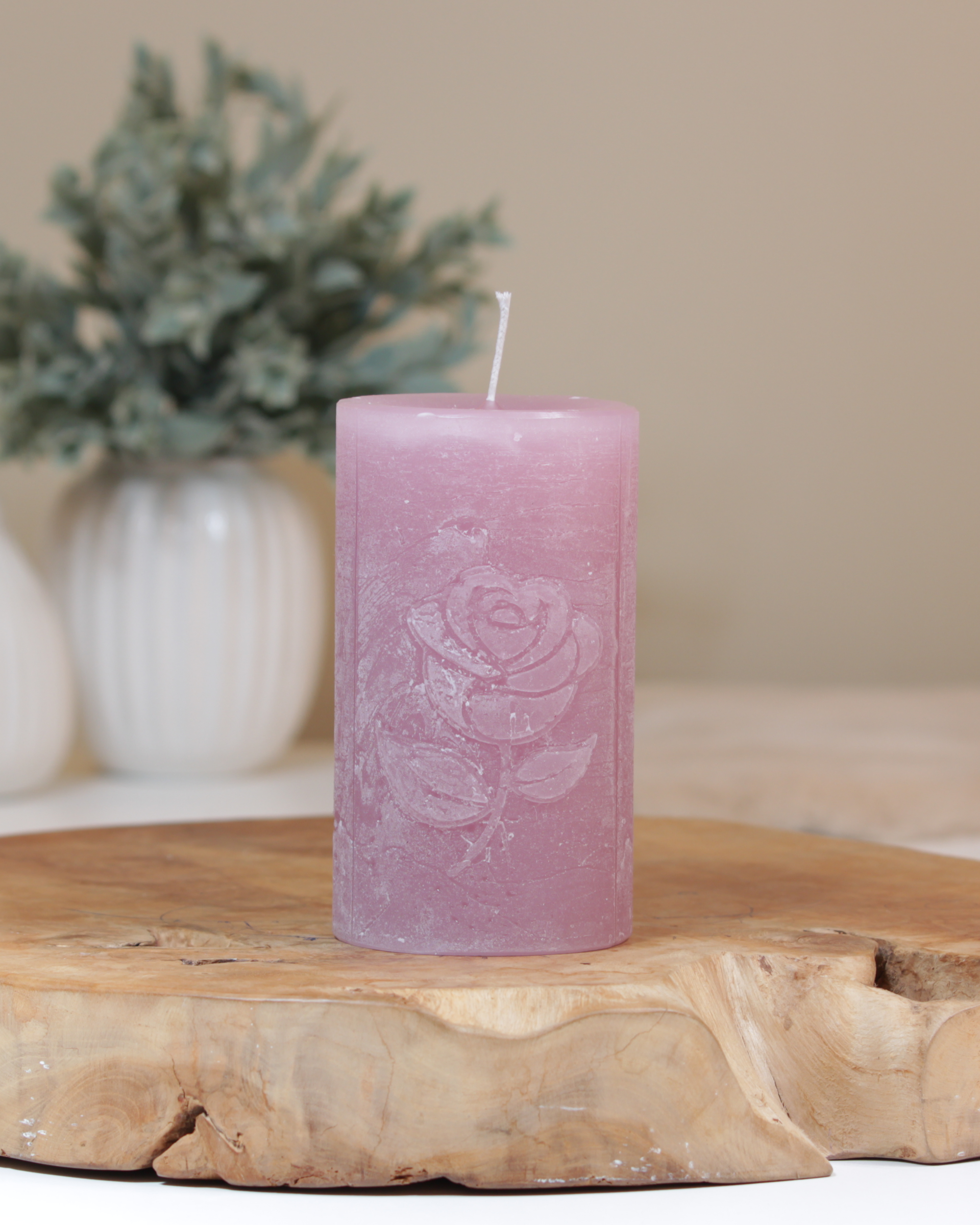 Rose Motivkerze in altrosa dekorativ auf einem Holztisch mit Pflanze im Hintergrund.