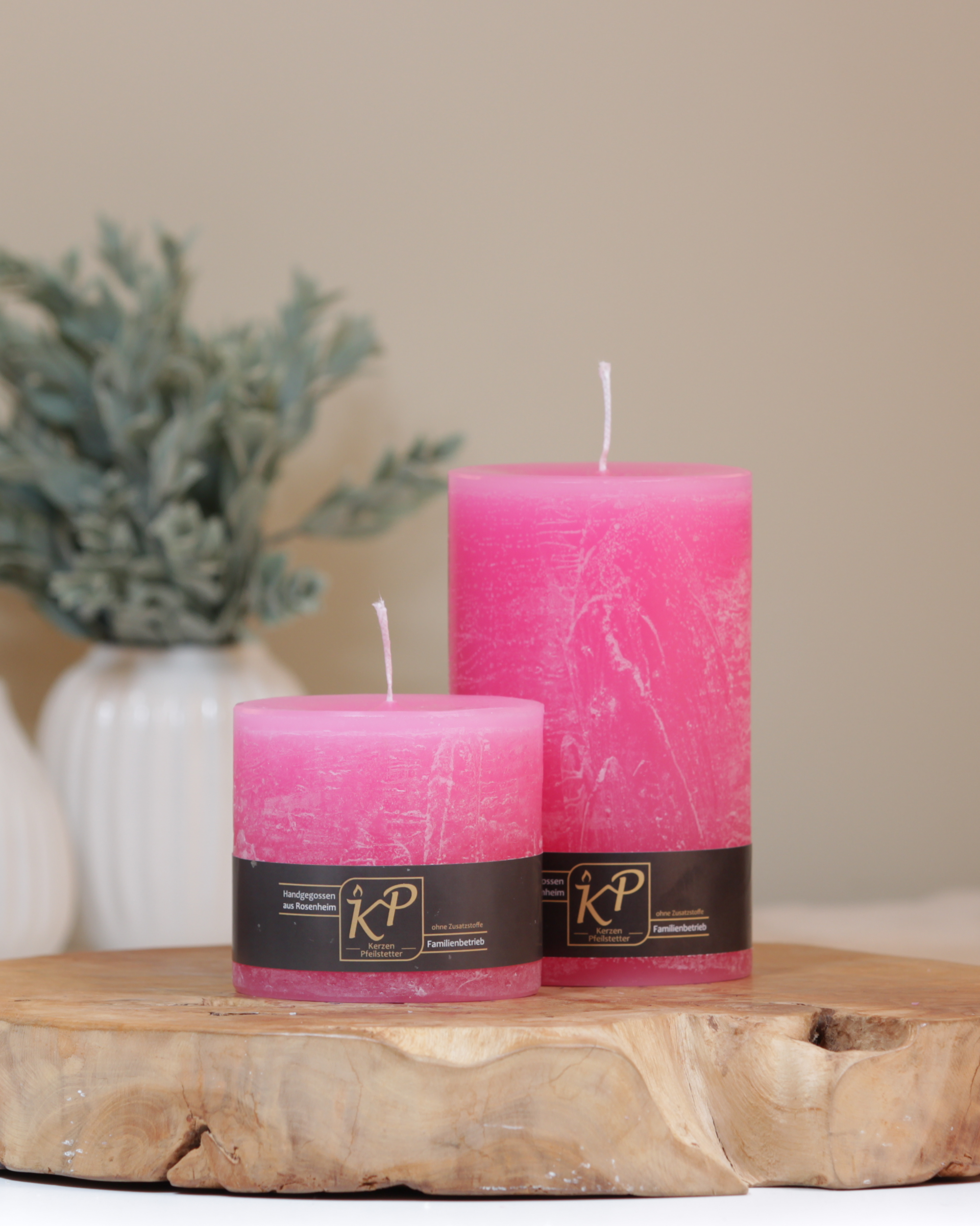 Stumpenkerzen in pink in zwei Größen – dekorativ auf einem Holztisch mit Pflanze im Hintergrund.