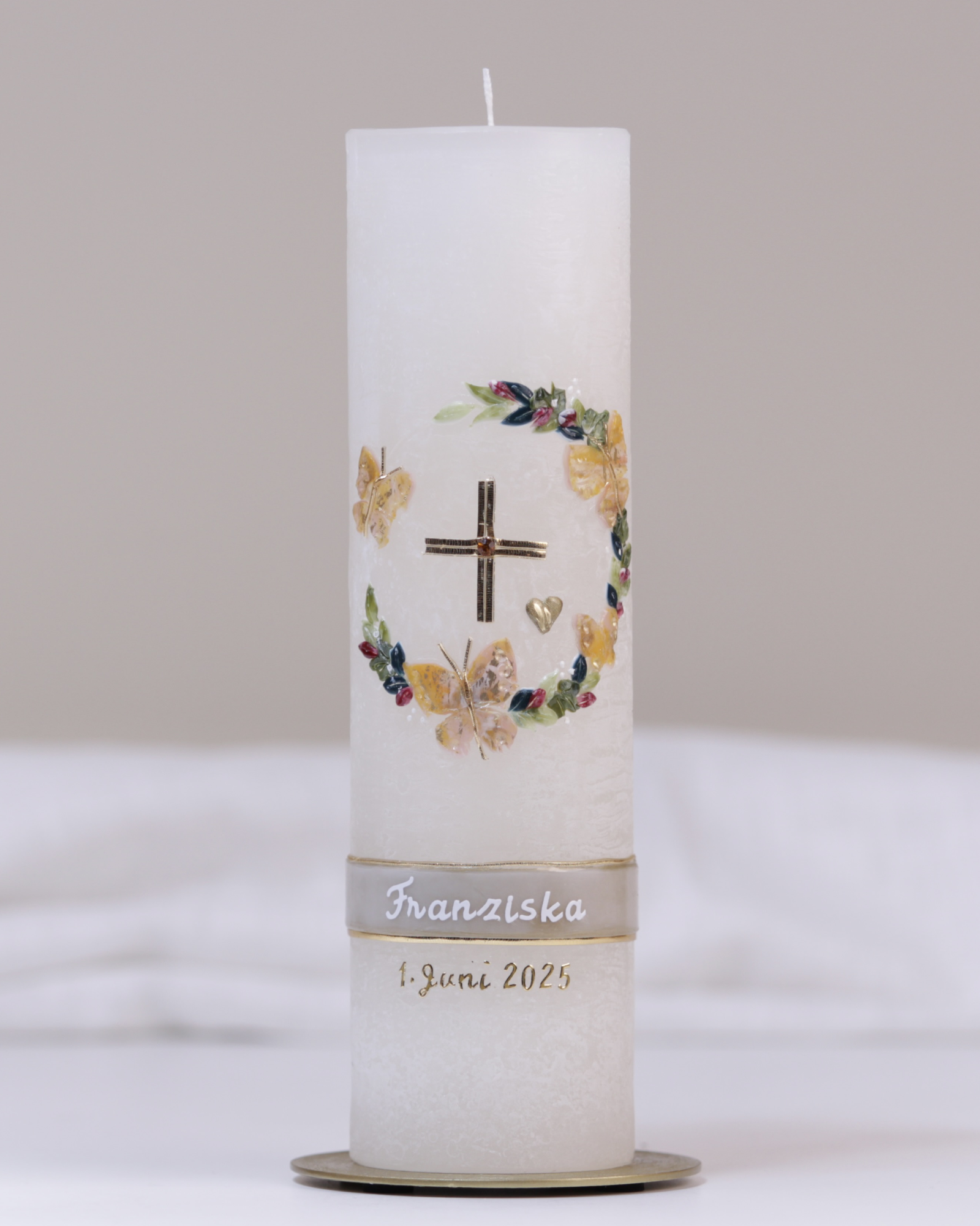 Elfenbeinfarbene Taufkerze mit gold-grüner Verzierung aus Kreuz, Herz, Blumenkranz und Schmetterlingen.