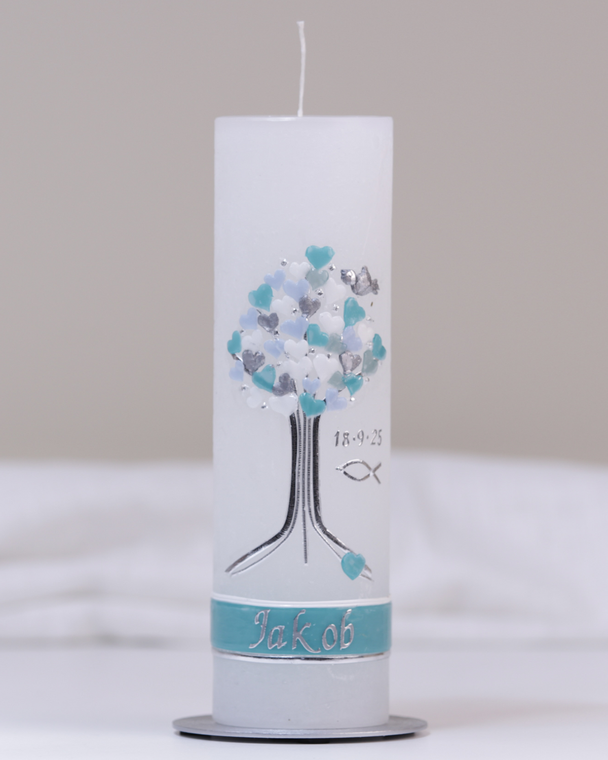 Weiße Taufkerze mit silber-blauer Verzierung aus Herzbaum und Fischsymbol.