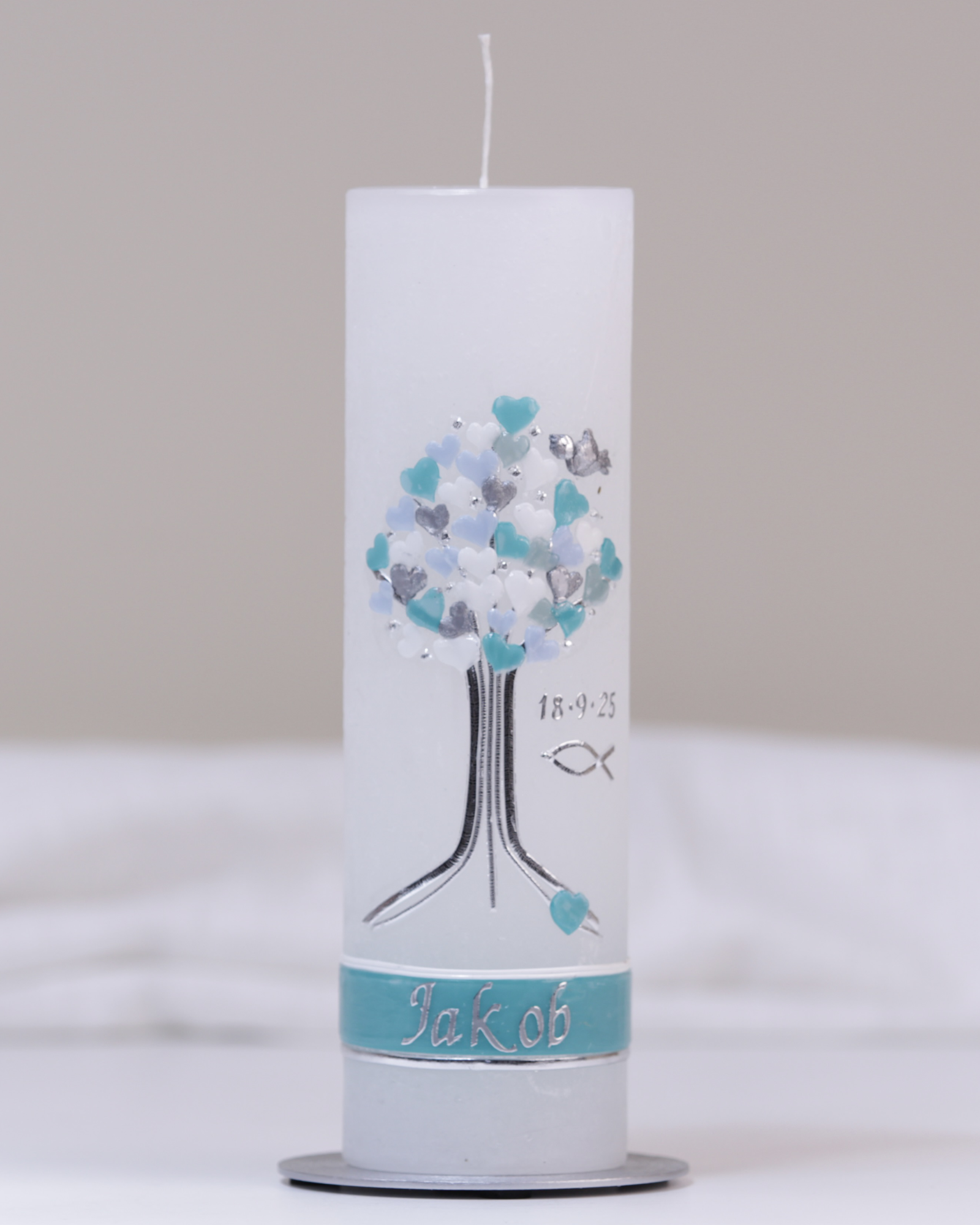 Weiße Taufkerze mit silber-blauer Verzierung aus Herzbaum und Fischsymbol.