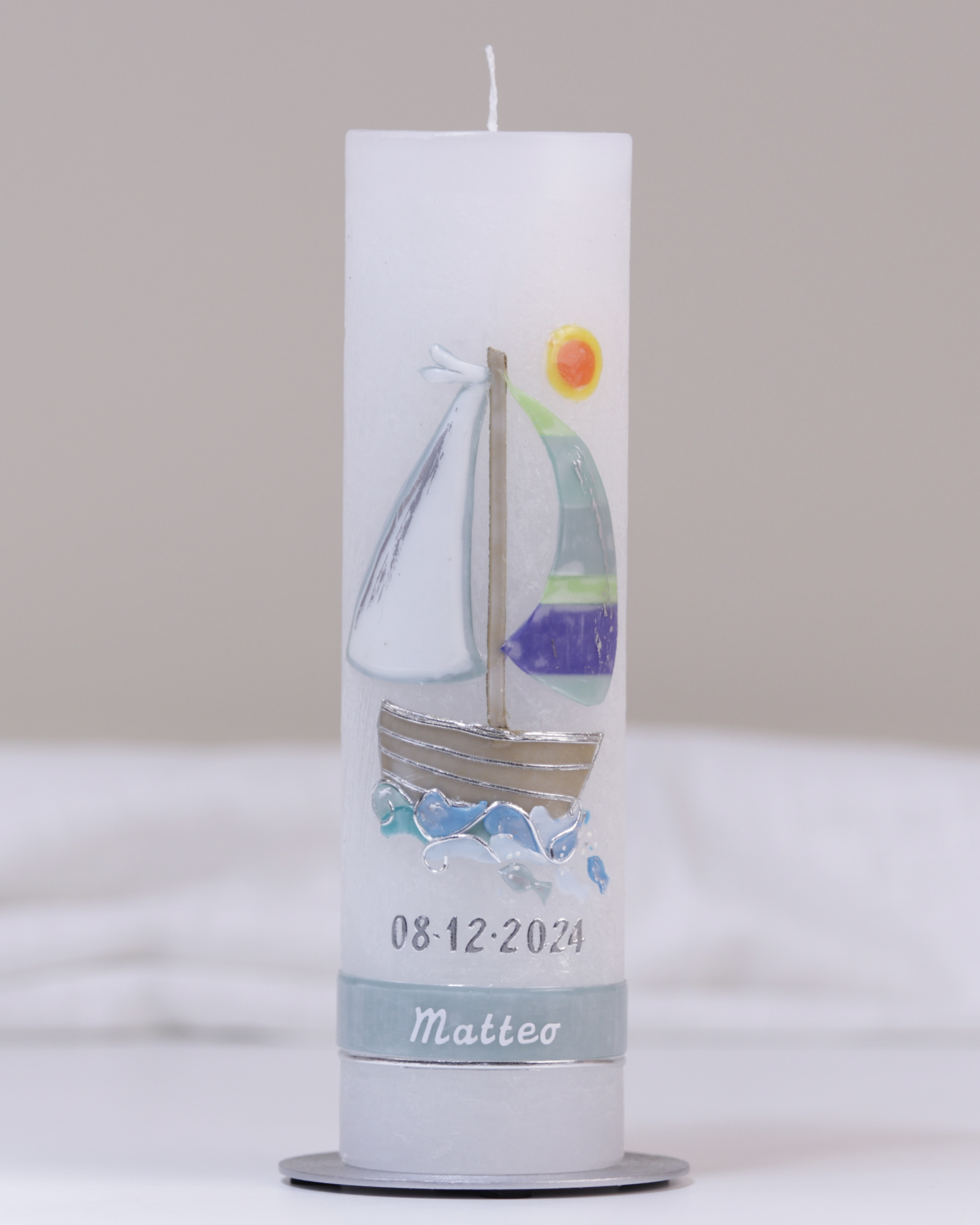 Weiße Taufkerze mit silber-blauer Verzierung aus handgeformtem Segelschiff und Sonne.