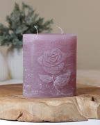 Zweidochtkerze mit Rose-Motiv in altrosa dekorativ auf einem Holztisch mit Pflanze im Hintergrund.