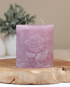 Zweidochtkerze mit Rose-Motiv in altrosa dekorativ auf einem Holztisch mit Pflanze im Hintergrund.
