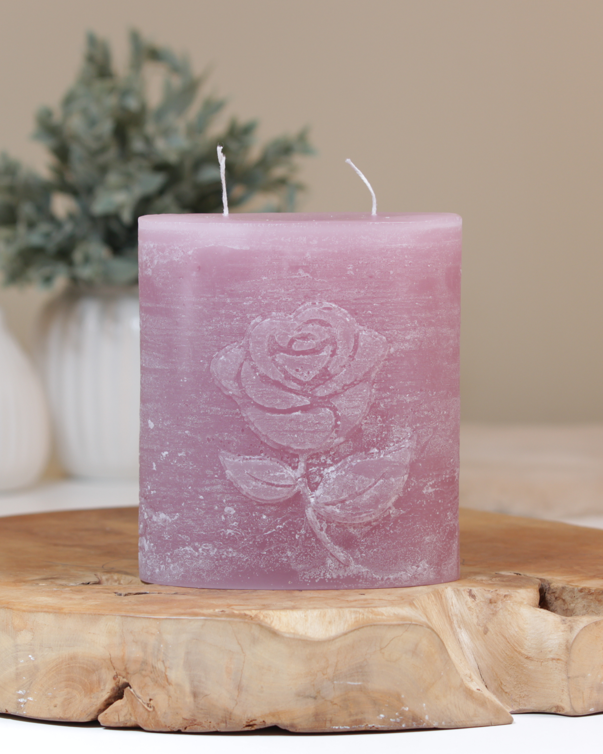 Zweidochtkerze mit Rose-Motiv in altrosa dekorativ auf einem Holztisch mit Pflanze im Hintergrund.